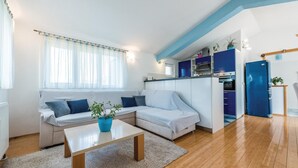 Ein modernes Wohnzimmer mit Sofa, Couchtisch und Küchenzeile inklusive Schränken und Geräten.
