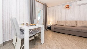 Ein gemütliches Wohnzimmer mit einem weißen Esstisch, einem grauen Sofa und einem Bild an der Wand.