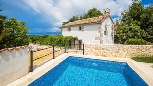 Une villa blanche avec un toit en tuiles, un mur en pierre et une piscine.