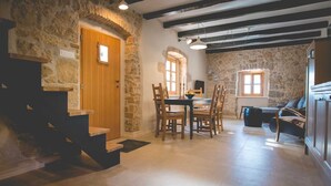 Un intérieur rustique avec un mur en pierre, un escalier en bois, un coin repas avec des chaises, une table et un canapé.