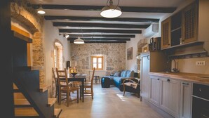 Une cuisine rustique aux murs de pierre, avec des poutres en bois et un coin repas comprenant une table et des chaises.