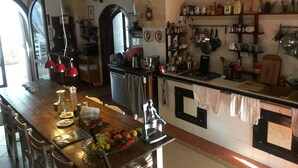 Een keuken met een houten eiland, diverse keukengerei en een scala aan pannen en servies op de muren.