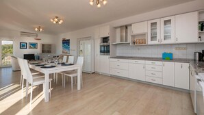 Een moderne keuken met witte kastjes, een eethoek met een witte tafel en stoelen, en een plafond met drie lampen.