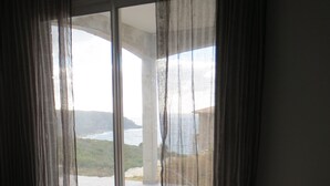 A bedroom with a large bed, sheer curtains, and a view of a coastal landscape.