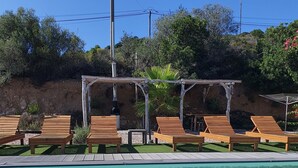 A clear blue pool with wooden lounge chairs and a pergola structure.
