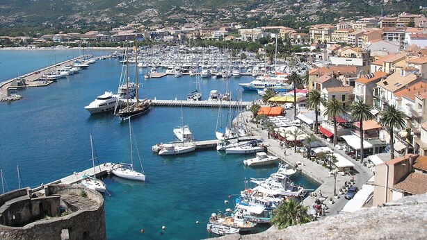 A coastal town with a marina filled with boats, surrounded by buildings and mountains. - Villa with pool, sea view, sleeps 6, tastefully decorated (Lumio)