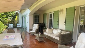 A covered patio area with wicker furniture, a sofa, and a table. - Villa with pool, sea view, sleeps 6, tastefully decorated (Lumio)