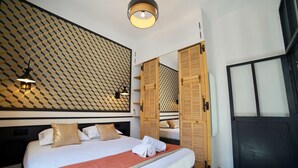 A hotel room with a large bed, a patterned wall, and a wardrobe with wooden doors. - Home Chic Home - Les Suites de La Comédie - Suite2 (Montpellier)