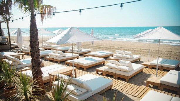 A beachside lounge area with wooden loungers, white cushions, and umbrellas providing shade. - Home Chic Home - Les Suites de La Comédie - Suite2 (Montpellier)