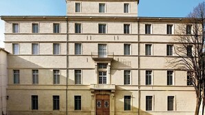 Un edifici gran de diverses plantes amb una façana simètrica, una entrada central amb una porta i un ample camí pavimentat que condueix a l'entrada.
