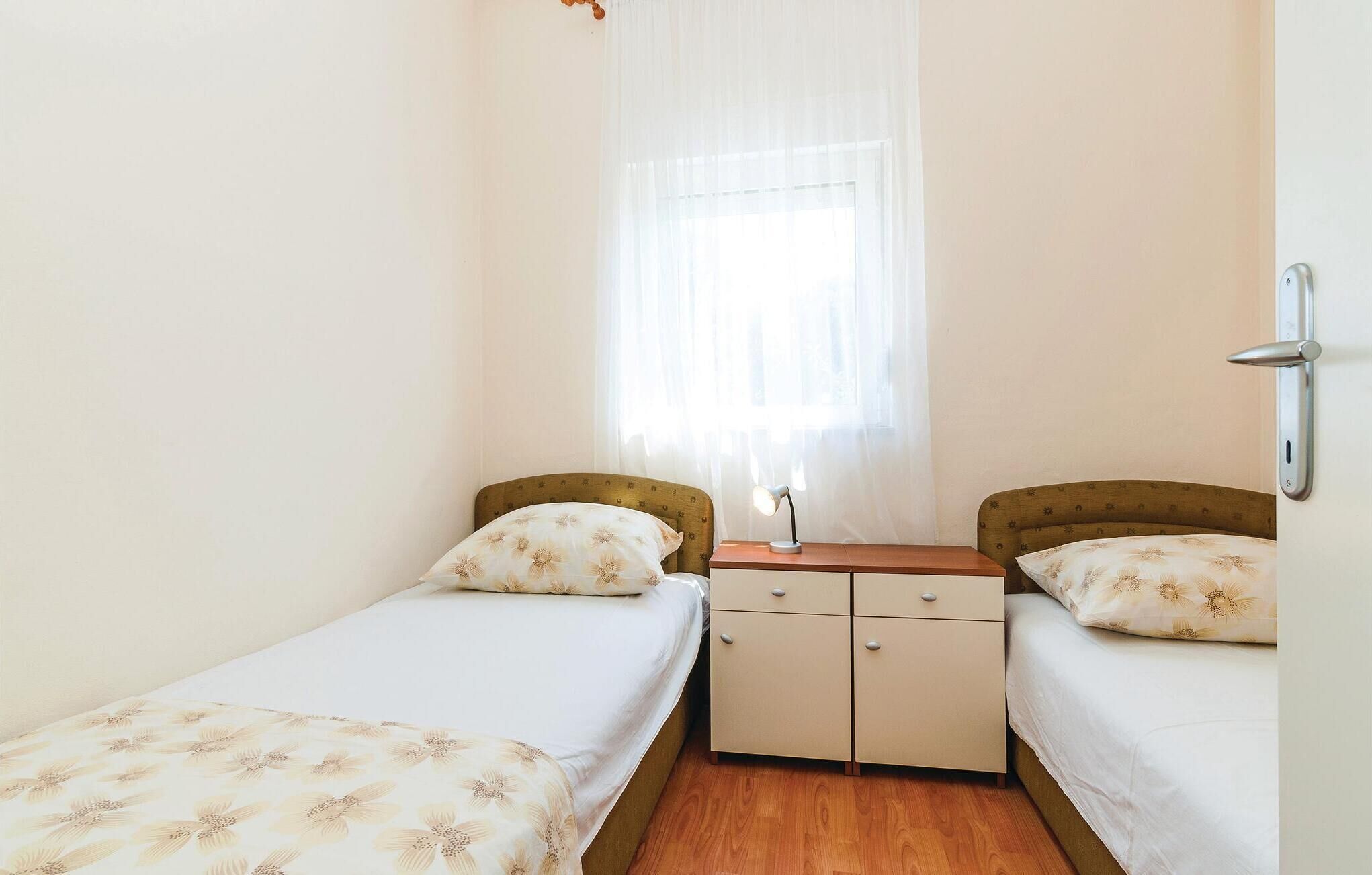 Ein kleines, helles Zimmer mit zwei Einzelbetten, einem Nachttisch mit Lampe und einem kleinen Schrank.