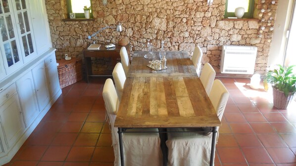 A dining area with a stone wall, a wooden table, and white chairs. - Charming Villa of 150m2 with swimming pool and garden near sea (Carry-Le-Rouet)