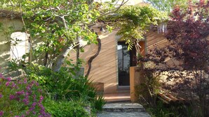 A garden entrance with a stone pathway leading to a door, surrounded by lush greenery and flowering plants. - Charming Villa of 150m2 with swimming pool and garden near sea (Carry-Le-Rouet)