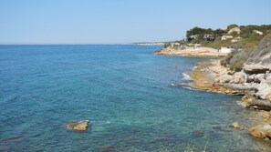 A coastal view with clear blue water, rocky shoreline, and houses on a hillside. - Charming Villa of 150m2 with swimming pool and garden near sea (Carry-Le-Rouet)