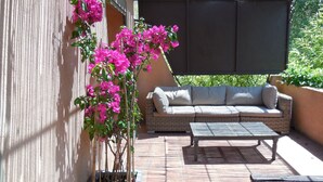 An outdoor seating area with a wicker sofa and a table, surrounded by a potted plant with pink flowers. - Charming Villa of 150m2 with swimming pool and garden near sea (Carry-Le-Rouet)