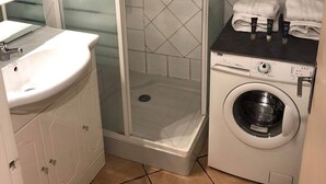 A bathroom with a glass-enclosed shower, a sink with a mirror, a washing machine, and a towel rack.