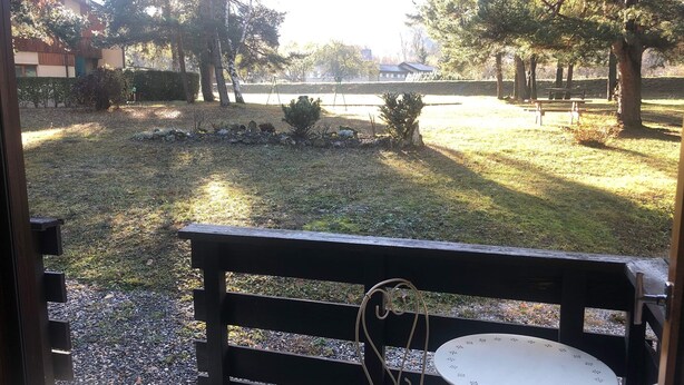 A wooden bench with a metal table and chair in a park area with trees and a grassy field.