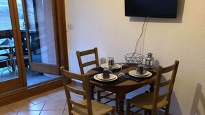 A dining area with a table set for four, wooden chairs, a TV mounted on the wall, and a sliding glass door leading to an outdoor area.