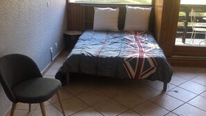 A small, cozy room with a bed, a chair, and a window overlooking a garden.
