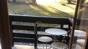A patio area with a table and chairs, a wooden fence, and a view of a park with trees and a building in the background.