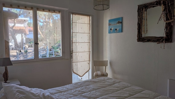 A bedroom with a bed, a window with a view of the outside, a painting on the wall, and a mirror. - Garden level apartment, for 5 persons, beach et lake 5 min away, great amenities (Soorts-Hossegor)