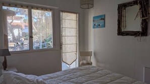 Une chambre à coucher avec un lit, une fenêtre donnant sur l’extérieur, un tableau accroché au mur et un miroir.