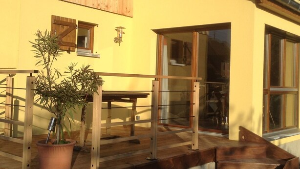 A yellow building with wooden siding, a balcony with a table and chairs, and a potted plant. - Le Gîtele: Cottage 7 people to Chatenois (Châtenois)