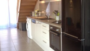 A modern kitchen with a black refrigerator, stainless steel appliances, and wooden beams on the ceiling. - Le Gîtele: Cottage 7 people to Chatenois (Châtenois)