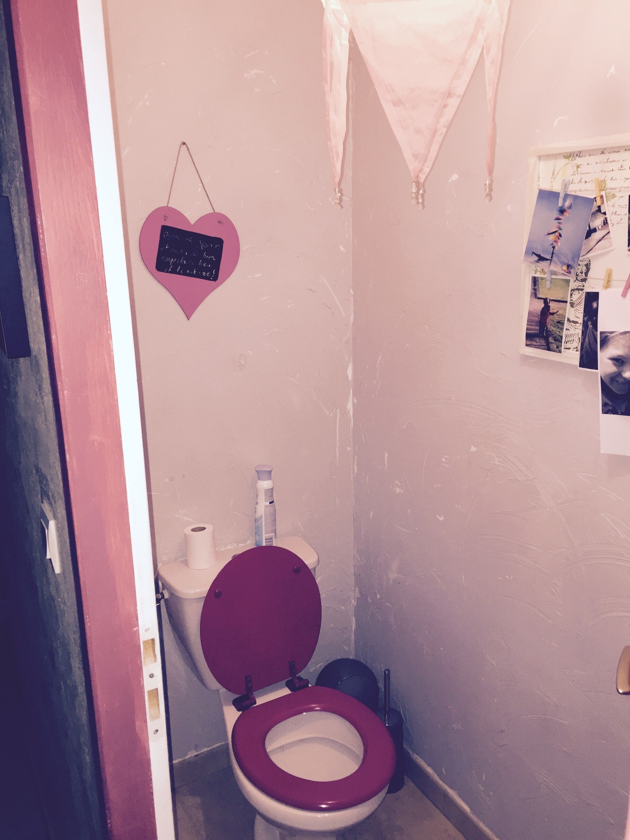 Un bagno con il water rosso, un lavandino bianco e una decorazione a forma di cuore rosa sulla parete.