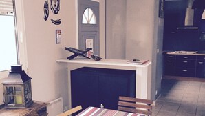 Un coin repas avec une nappe à rayures, des chaises en bois, une petite table sur laquelle est posée une lanterne, et une cuisine en arrière-plan.