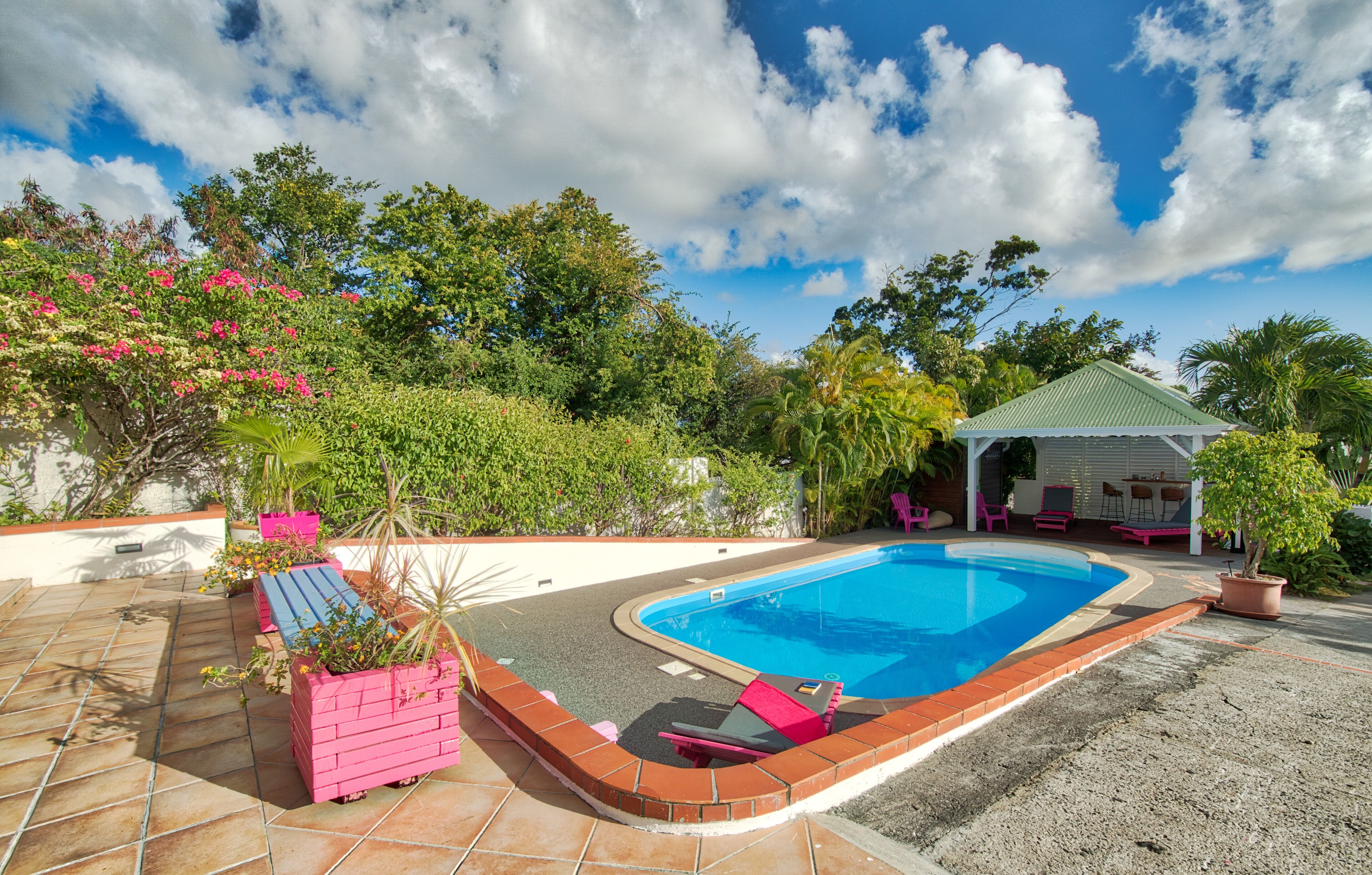 A swimming pool with a tiled deck, surrounded by potted plants and a gazebo.
