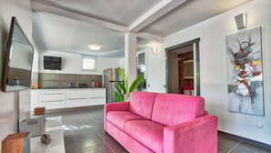 Un salon moderne avec un canapé rose, un téléviseur à écran plat et un grand tableau abstrait.