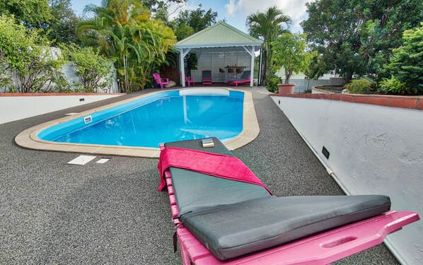 A swimming pool with lounge chairs and a covered seating area. - A bright and spacious flat, balneo-swimming pool, between sea and countryside (SAINTE-ANNE)