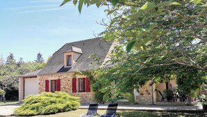 A stone house with a sloped roof, red shutters, and a small attached garage. There are two lounge chairs in the front yard. - Périgourdine gîte (air-conditioned) 5kms from SARLAT, enclosed grounds. (Carsac-Aillac)