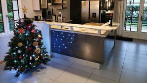 A modern kitchen with a central island, pendant lighting, and a decorated Christmas tree. - Périgourdine gîte (air-conditioned) 5kms from SARLAT, enclosed grounds. (Carsac-Aillac)