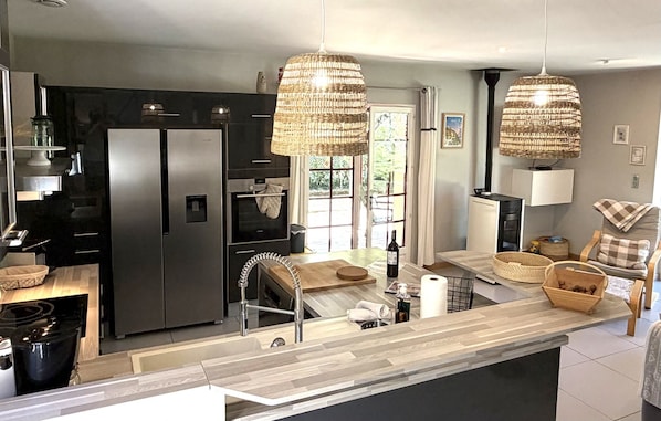 Cozinha moderna com ilha central, eletrodomésticos de aço inoxidável e luminárias pendentes de vime.