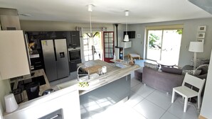 A modern kitchen with a central island, built-in appliances, and a dining area with a sofa and chairs. - Périgourdine gîte (air-conditioned) 5kms from SARLAT, enclosed grounds. (Carsac-Aillac)