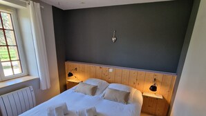 A neatly made bed with white linens and pillows, a wooden headboard, bedside lamps, and a window with curtains. - Périgourdine gîte (air-conditioned) 5kms from SARLAT, enclosed grounds. (Carsac-Aillac)