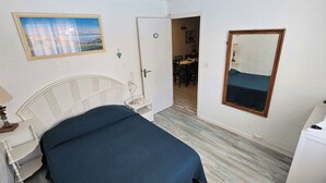Een slaapkamer met een bed, nachtkastje met lamp, een kaptafel, een spiegel en een deur naar een eetgedeelte.