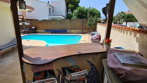 Een zwembadgedeelte met een houten terras, een ligstoel en een tafeltje.
