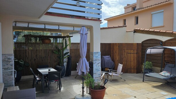 Een terras met een tafel en stoelen, een overdekte zithoek en een houten omheining.