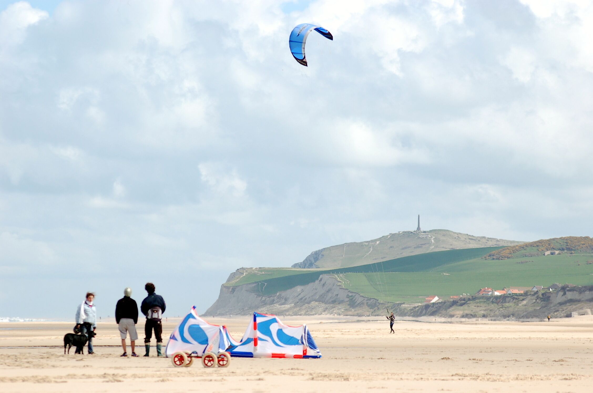 A beach with a kite, tents, and a hill in the background.
