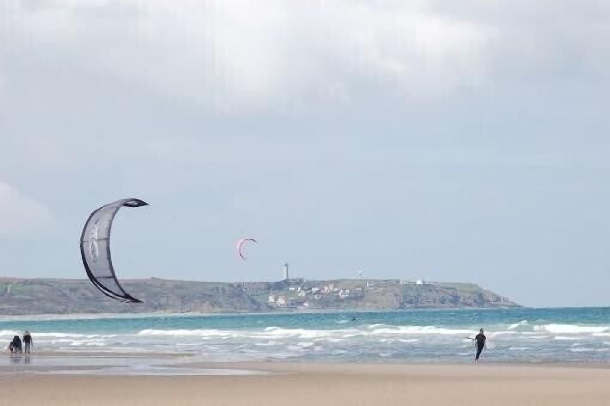 Une plage avec un phare en arrière-plan et des personnes près de l’eau.