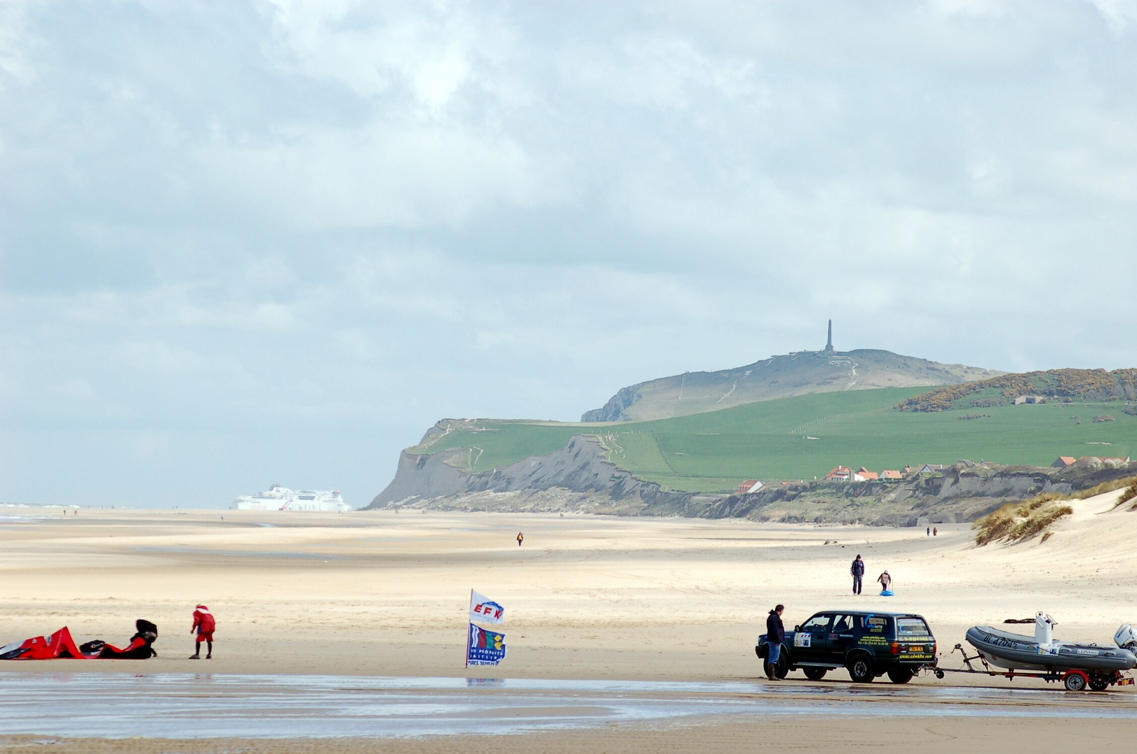 A beach with a flag, a truck, and a boat.