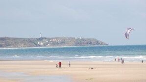 Una playa con un faro al fondo y una cometa en el cielo.