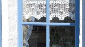 Una ventana con detalles azules, encaje blanco y dos macetas con flores.