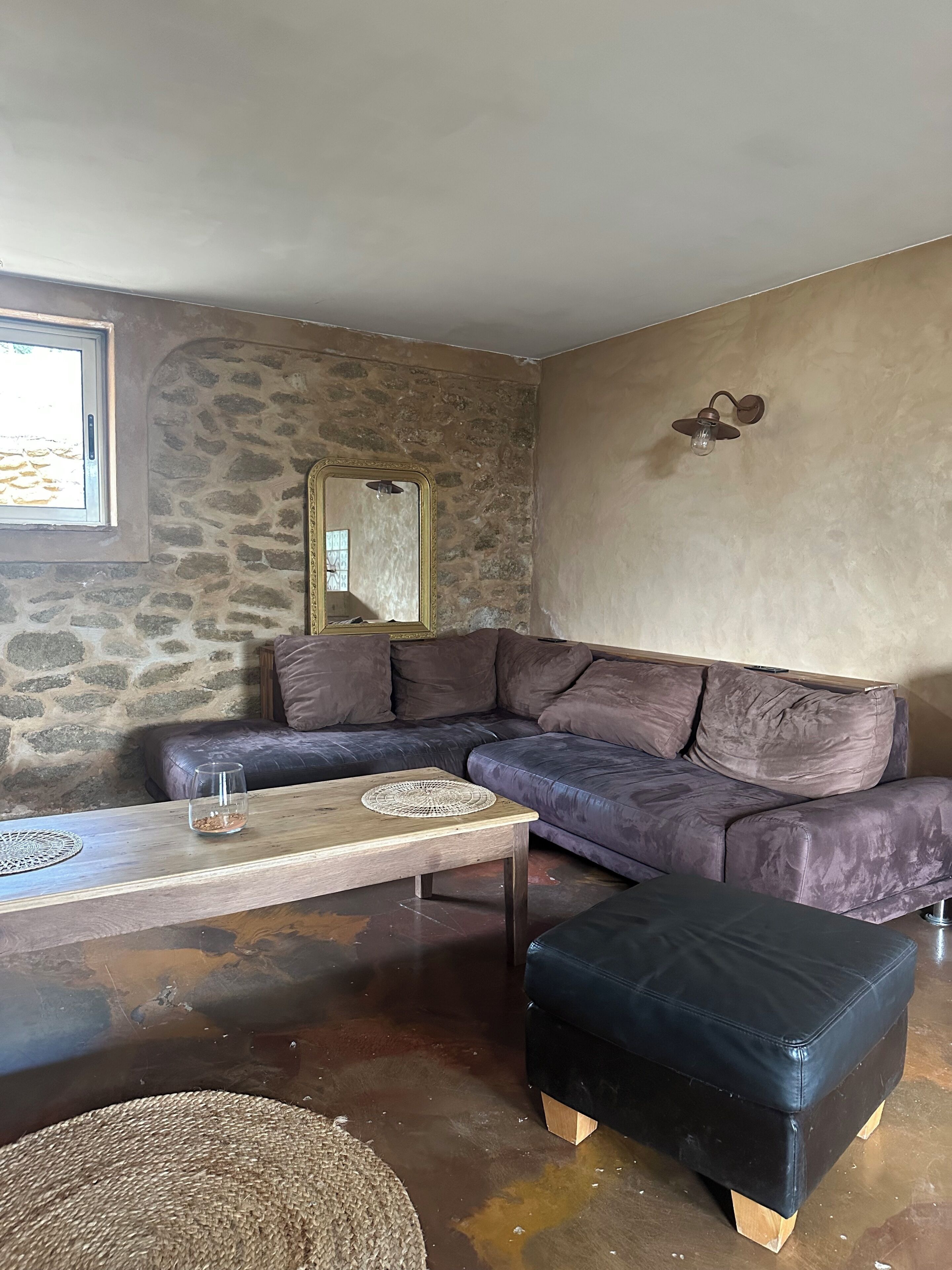 A living room with a stone wall, a large mirror, a dark leather sofa, a wooden coffee table, and a black ottoman.