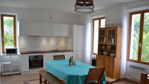 A kitchen with white cabinets, a wooden dining table with a teal tablecloth, and a built-in oven. - TYPICAL VILLAGE HOUSE CORSE  (Levie)