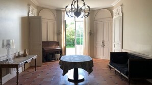 A spacious room with a round table, a piano, a sofa, and a chandelier. - CHARTER OF YESTERYEAR (Sainte-Eulalie)