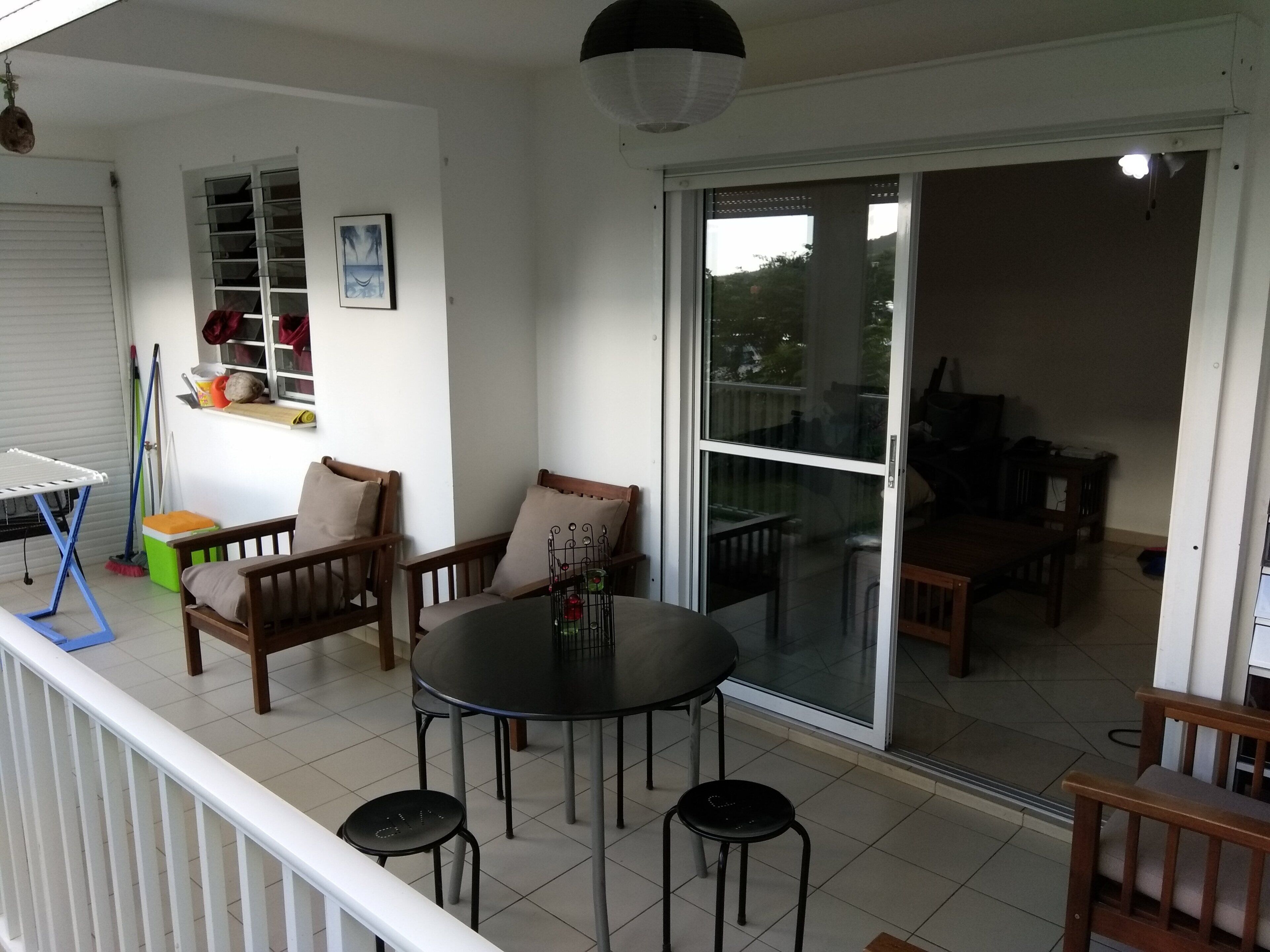 Ein Balkon mit Tisch und Stühlen, eine Schiebetür und Blick auf den Garten.
